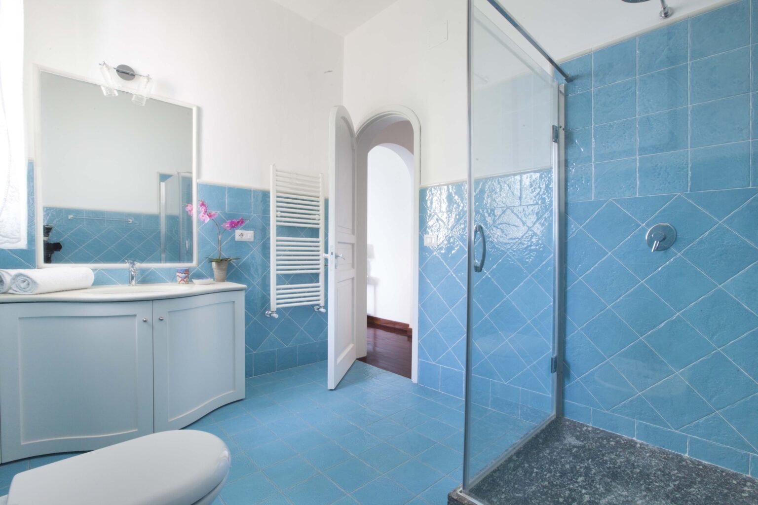 Modern bathroom in a luxury villa for rent in Italy, featuring blue tiled walls, a spacious shower, and elegant fixtures, highlighting a serene and upscale atmosphere. | Only on SopranoVillas