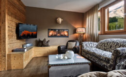 Cozy living room featuring a modern design with wooden accents, a wall-mounted TV, a stylish sofa, and a coffee table. Large windows offer a scenic view of the mountains, enhancing the inviting atmosphere of the space.