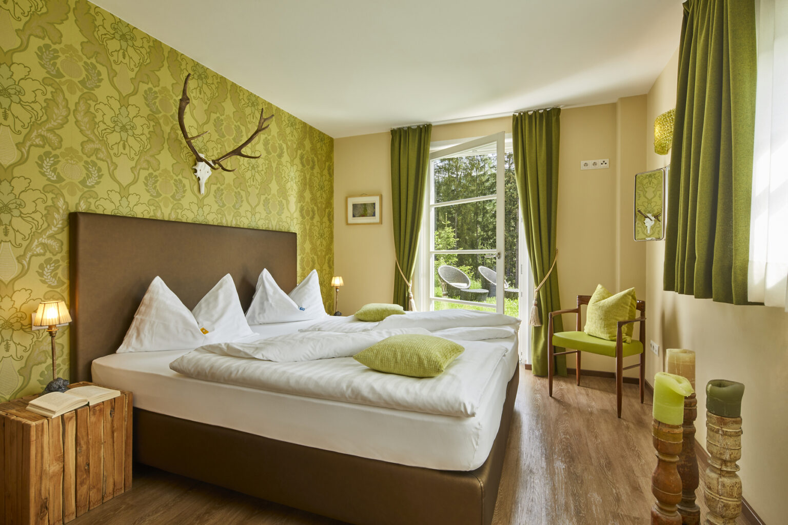 Cozy hotel bedroom featuring two beds with white linens and green accent pillows, adorned with a stylish green wallpaper, wooden furniture, and large windows allowing natural light. Ideal for a relaxing stay. | Only on SopranoVillas