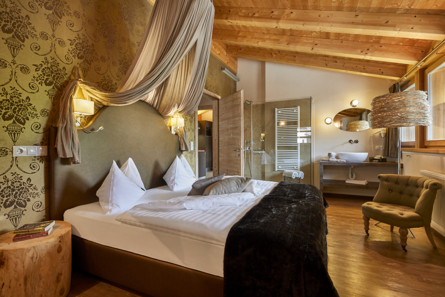 Cozy and elegant hotel room featuring a king-sized bed with plush pillows, warm wooden accents, and stylish decor. Includes a modern bathroom area with glass partitions and a comfortable seating area, ideal for relaxation. | Only on SopranoVillas