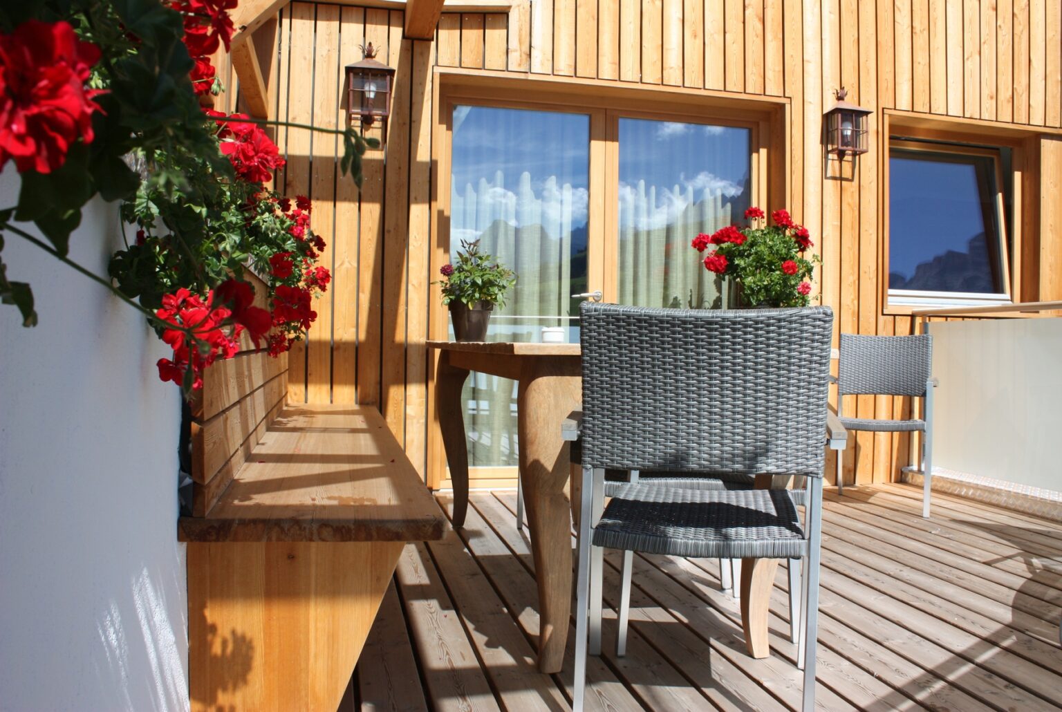 Cozy balcony with wooden paneling, featuring potted red geraniums and a small table with chairs, ideal for relaxation and enjoying outdoor views. | Only on SopranoVillas