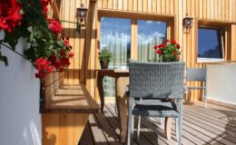 Cozy balcony with wooden paneling, featuring potted red geraniums and a small table with chairs, ideal for relaxation and enjoying outdoor views.