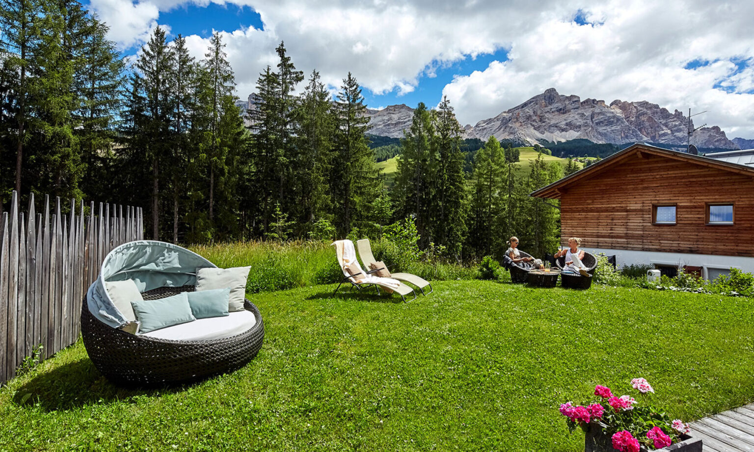 Cozy outdoor seating area with modern lounge chairs and a circular sofa on a lush green lawn, surrounded by tall trees and stunning mountain views under a partly cloudy sky. Ideal for relaxation and enjoying nature. | Only on SopranoVillas