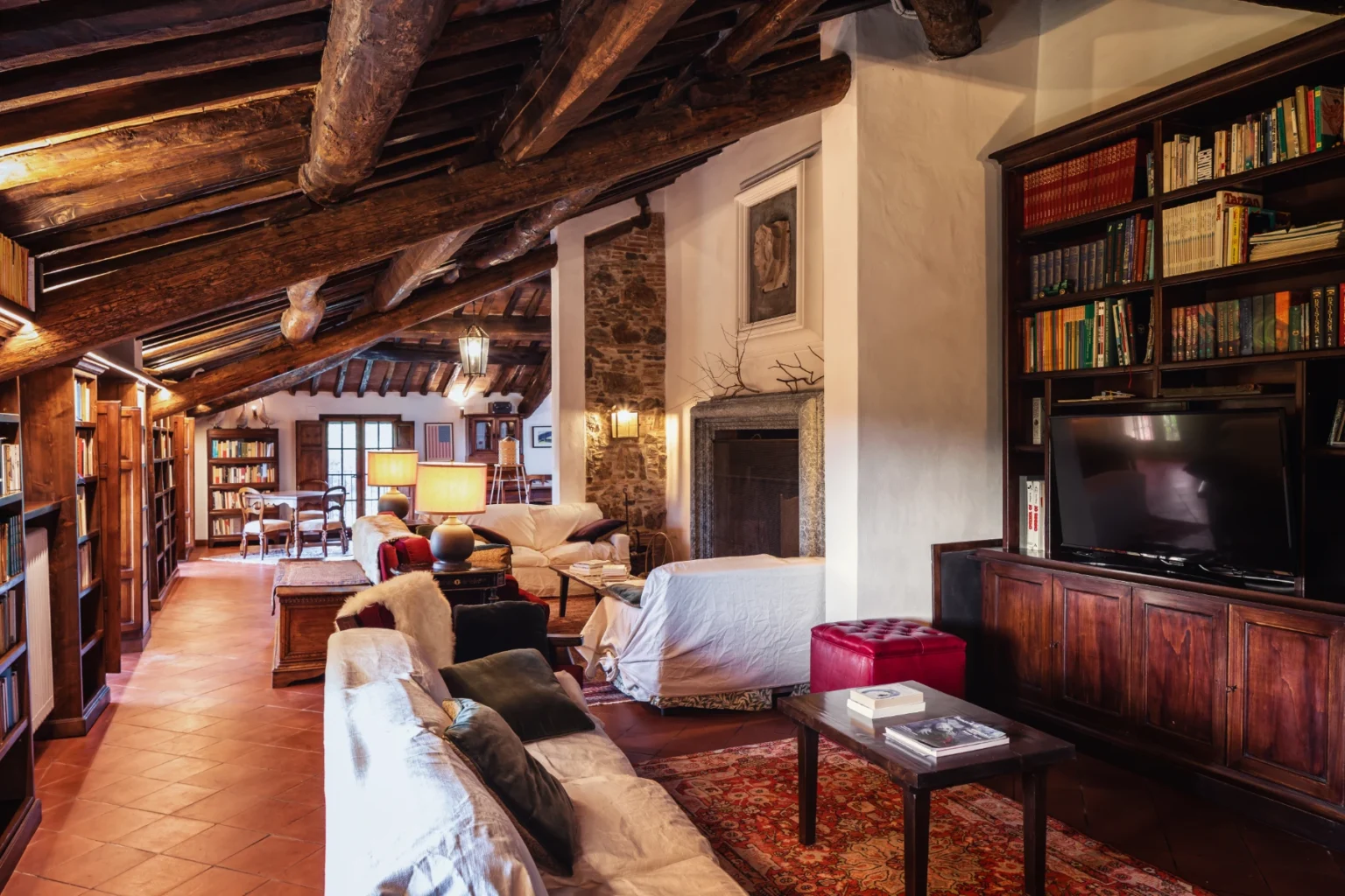 Cozy living room with wooden beams, a fireplace, and a large bookshelf, featuring comfortable seating and warm lighting. Ideal for relaxation and reading. | Only on SopranoVillas