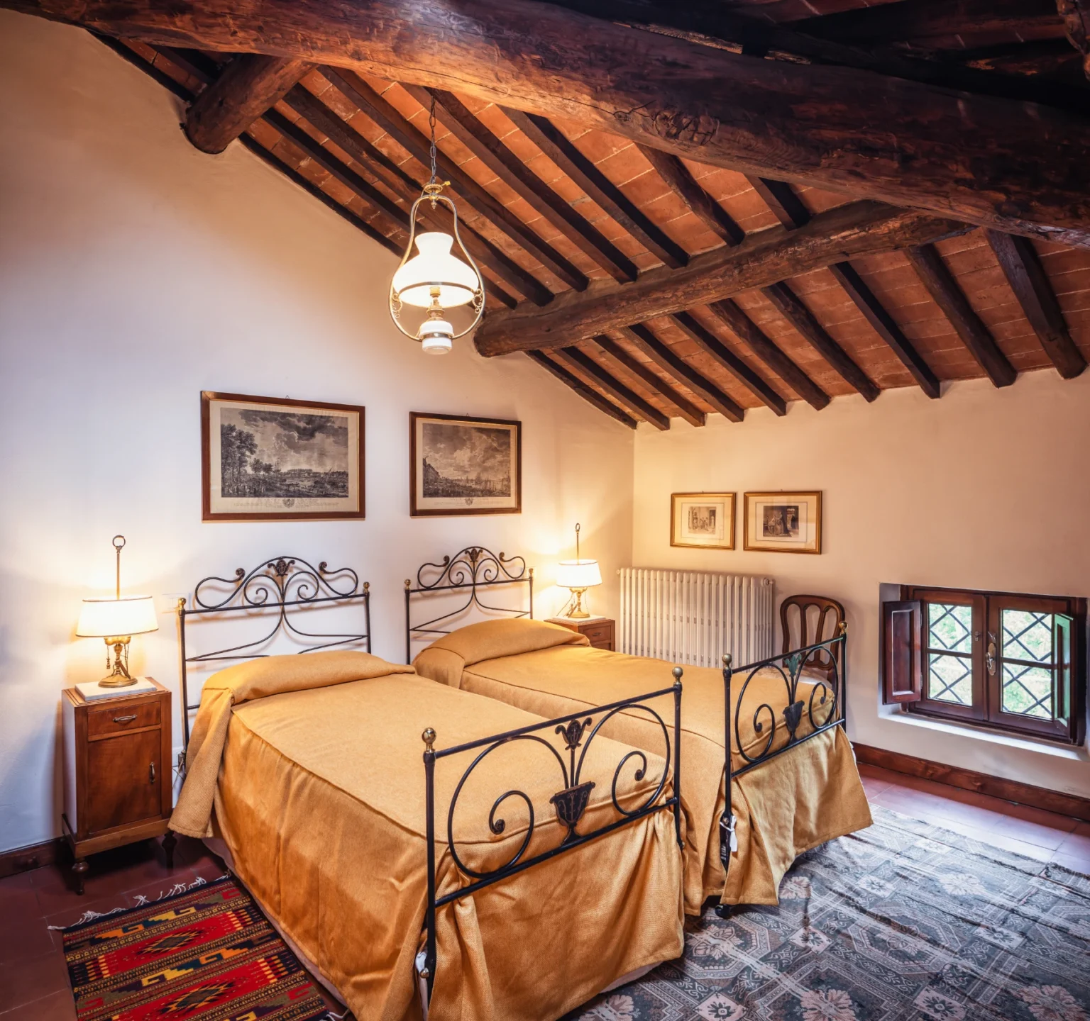 Cozy guest room featuring two wrought iron beds with yellow bedding, wooden beamed ceiling, vintage wall art, and warm lighting from bedside lamps. | Only on SopranoVillas