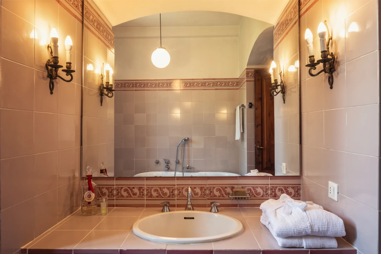 Elegant bathroom interior featuring a vintage bathtub, stylish wall sconces, and a large mirror, complemented by soft towels for a luxurious ambiance. | Only on SopranoVillas