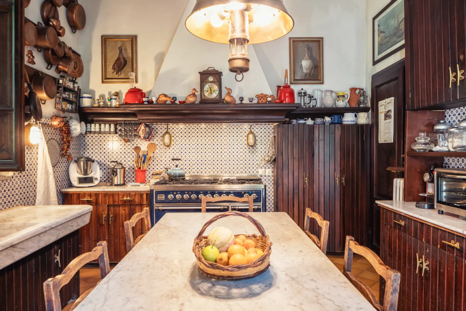 Rustic kitchen interior featuring a marble dining table with a fruit basket, wooden cabinetry, vintage decor, and a large stove, creating a warm and inviting atmosphere. | Only on SopranoVillas