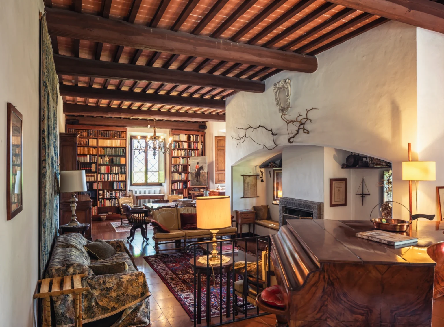 Cozy living room featuring wooden beams, a fireplace, bookshelves filled with books, elegant furniture, and warm lighting, creating a welcoming atmosphere. | Only on SopranoVillas