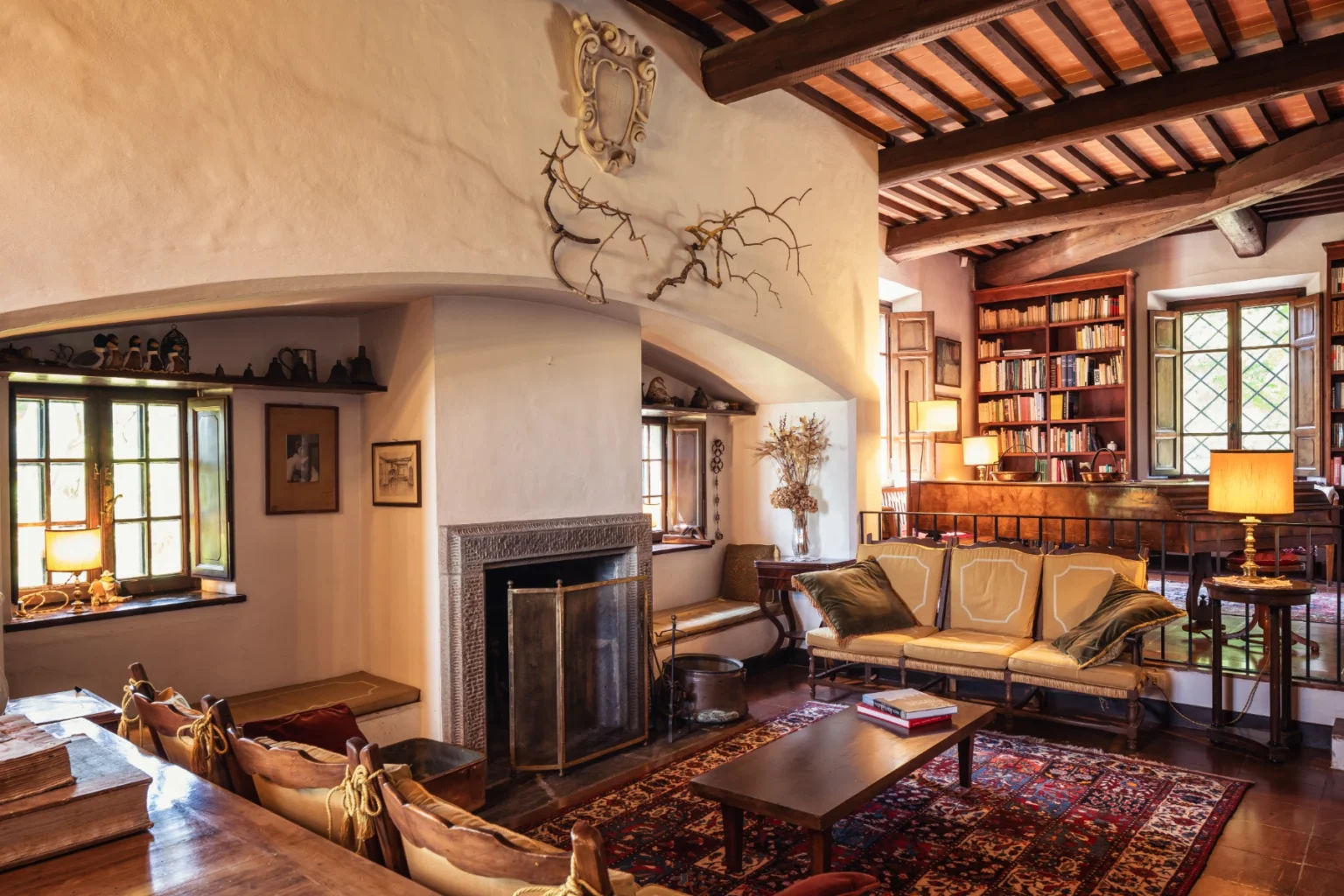 Cozy living room featuring a rustic design with wooden beams, a stone fireplace, and a comfortable sofa. The room is adorned with bookshelves, warm lighting, and decorative elements, creating an inviting atmosphere. | Only on SopranoVillas