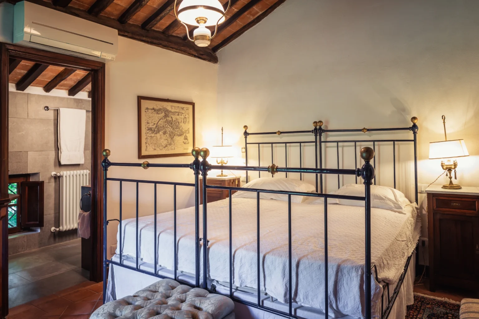 Cozy bedroom featuring a vintage iron bed, warm lighting from bedside lamps, and rustic wooden beams on the ceiling, creating a charming and inviting atmosphere. | Only on SopranoVillas
