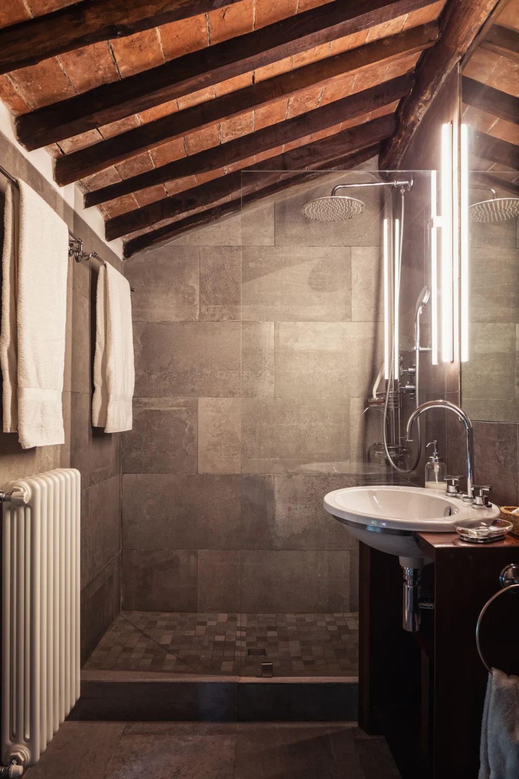 Modern bathroom interior featuring a sleek sink, contemporary lighting, and stylish gray tile walls, complemented by neatly hung towels and a radiator. | Only on SopranoVillas