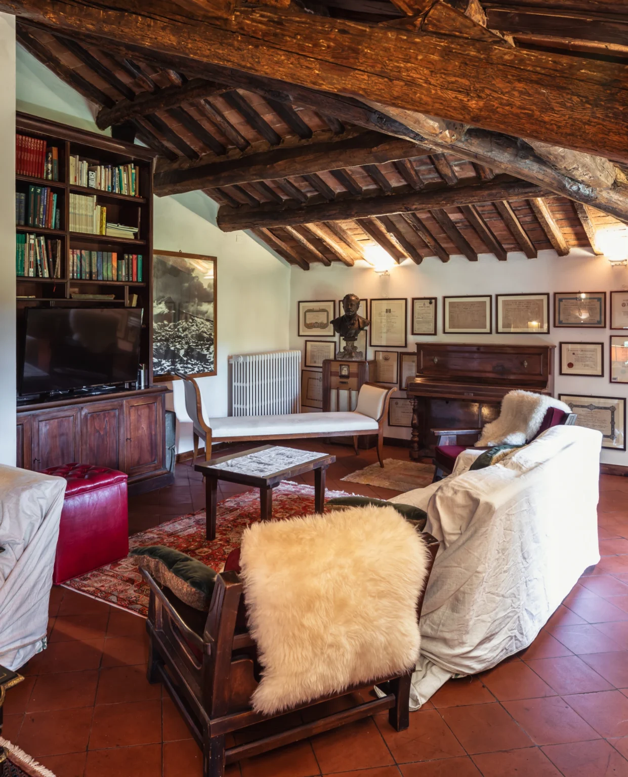Cozy living room featuring a rustic wooden ceiling, comfortable seating, a vintage piano, and framed artwork on the walls, creating an inviting atmosphere for relaxation and entertainment. | Only on SopranoVillas