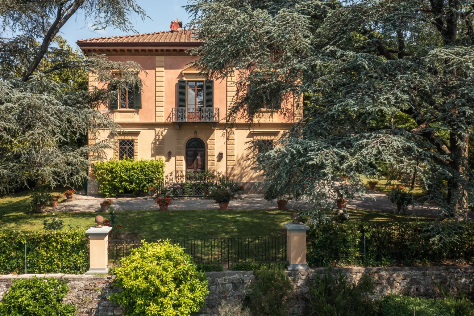 Elegant two-story villa surrounded by lush greenery and well-maintained gardens, featuring classic architecture with large windows and a welcoming entrance. Ideal for showcasing residential properties or landscape design. | Only on SopranoVillas