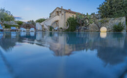 Serene outdoor pool reflecting a charming villa surrounded by lush greenery and modern seating, capturing a tranquil sunset ambiance.