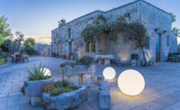 Stone building with lush greenery and decorative glowing orbs in a tranquil outdoor setting at dusk.