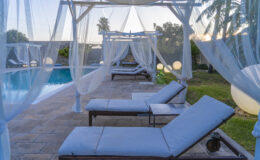 Relaxing outdoor pool area with lounge chairs and sheer canopies, surrounded by lush greenery and palm trees, perfect for leisure and comfort.