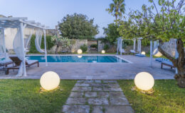 Modern backyard oasis featuring a swimming pool surrounded by lounge chairs, illuminated by decorative globes, with lush greenery and a tranquil atmosphere. Ideal for relaxation and outdoor gatherings.