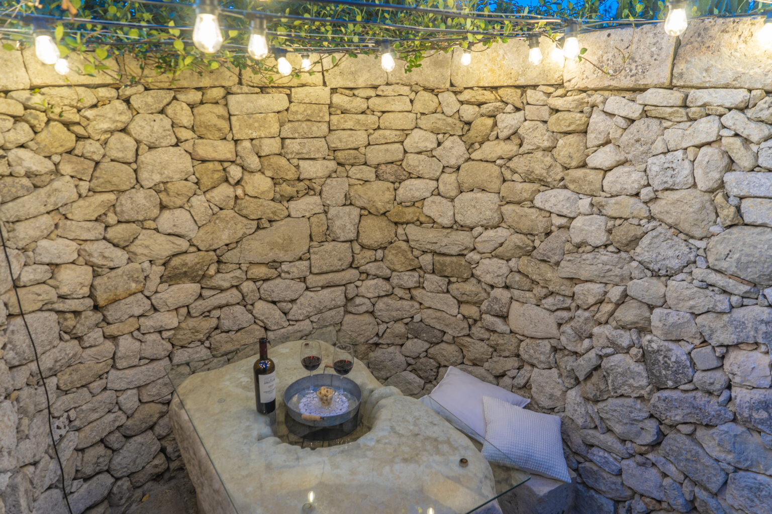 Cozy outdoor dining area with stone walls, soft lighting, a bottle of wine, and two glasses, creating a romantic atmosphere. | Only on SopranoVillas