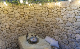 Cozy outdoor dining area with stone walls, soft lighting, a bottle of wine, and two glasses, creating a romantic atmosphere.