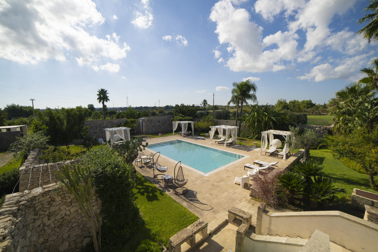 Beautiful outdoor pool surrounded by lush greenery and palm trees, featuring comfortable lounge chairs and shaded cabanas under a clear blue sky. Ideal for relaxation and leisure. | Only on SopranoVillas