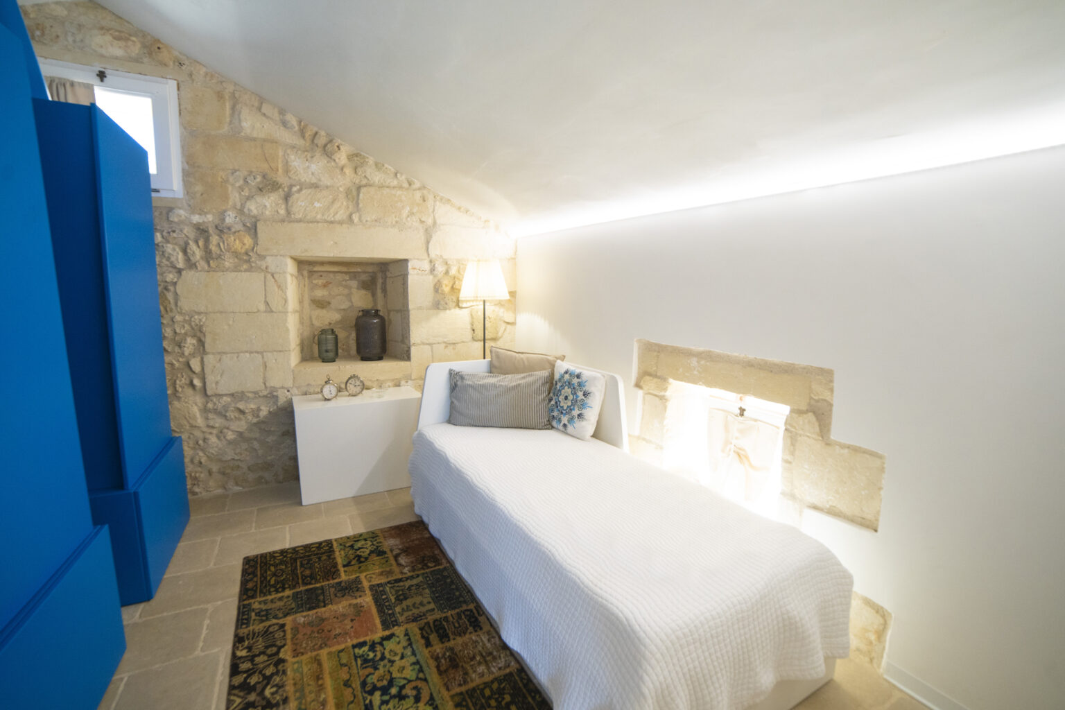 Cozy bedroom featuring a single bed, stone wall accents, modern lighting, and a decorative rug, ideal for a minimalist and stylish retreat. | Only on SopranoVillas