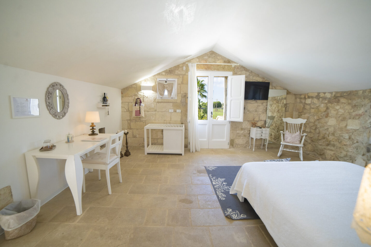 Cozy and modern bedroom featuring stone walls, a white bed, a stylish desk, and natural light from large windows, ideal for a relaxing getaway. | Only on SopranoVillas