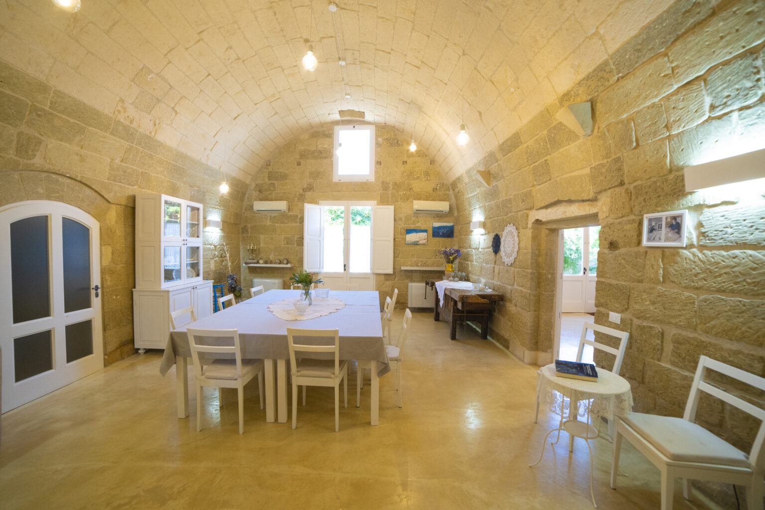 Spacious dining area with high arched stone ceilings, featuring a large table surrounded by white chairs, natural light streaming through windows, and tasteful decor. | Only on SopranoVillas