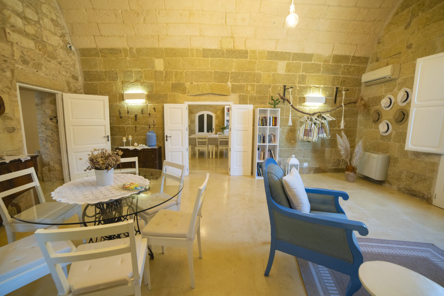 Bright and spacious interior of a rustic-style living room featuring stone walls, a glass dining table, blue accent chairs, and decorative wall plates, ideal for cozy gatherings. | Only on SopranoVillas