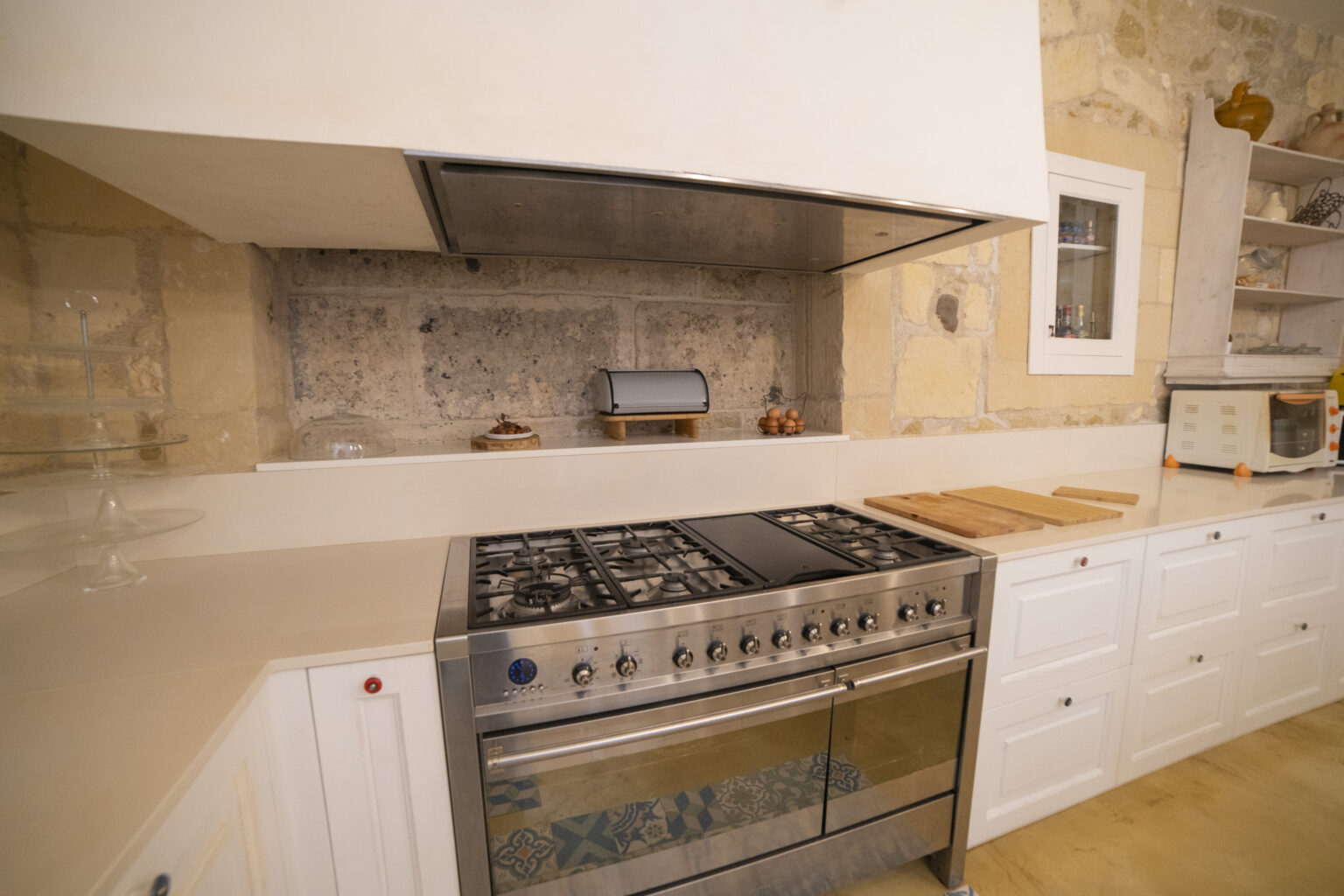 Modern kitchen featuring a stainless steel gas range, white cabinetry, and a stone accent wall. A wooden cutting board and a microwave are visible, enhancing the functional and stylish design of the space. | Only on SopranoVillas