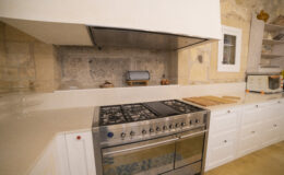 Modern kitchen featuring a stainless steel gas range, white cabinetry, and a stone accent wall. A wooden cutting board and a microwave are visible, enhancing the functional and stylish design of the space.