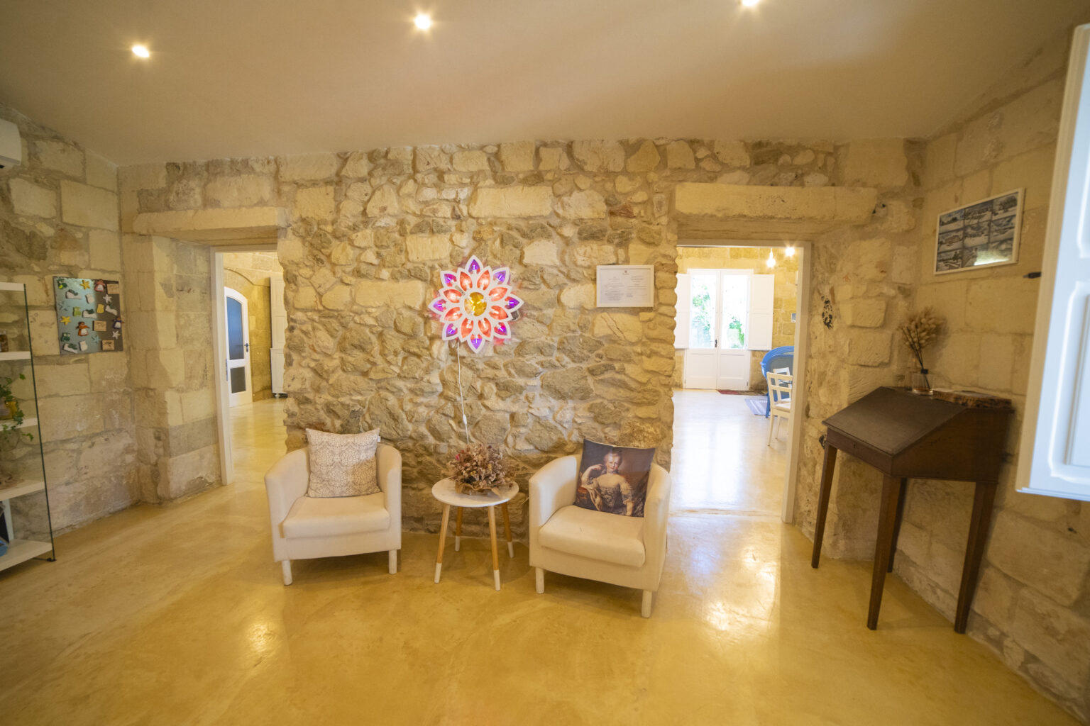 Cozy interior of a stone-walled living space featuring two armchairs, a small table, and decorative wall art. Natural lighting enhances the warm ambiance, creating an inviting atmosphere. | Only on SopranoVillas