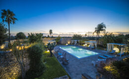 Luxurious outdoor pool area at sunset, featuring palm trees, landscaped gardens, and illuminated seating, perfect for relaxation and entertainment.