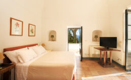 Spacious and bright bedroom featuring a king-size bed, wooden furniture, a flat-screen TV, and large windows with scenic views, perfect for a relaxing stay.