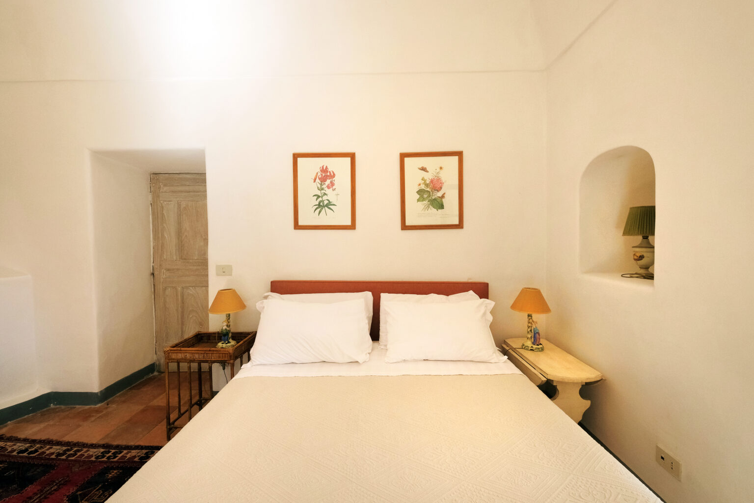 Cozy bedroom featuring a comfortable bed with white linens, two decorative lamps, and floral artwork on the walls, set in a bright, minimalist space. | Only on SopranoVillas