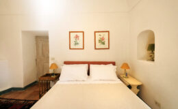 Cozy bedroom featuring a comfortable bed with white linens, two decorative lamps, and floral artwork on the walls, set in a bright, minimalist space.