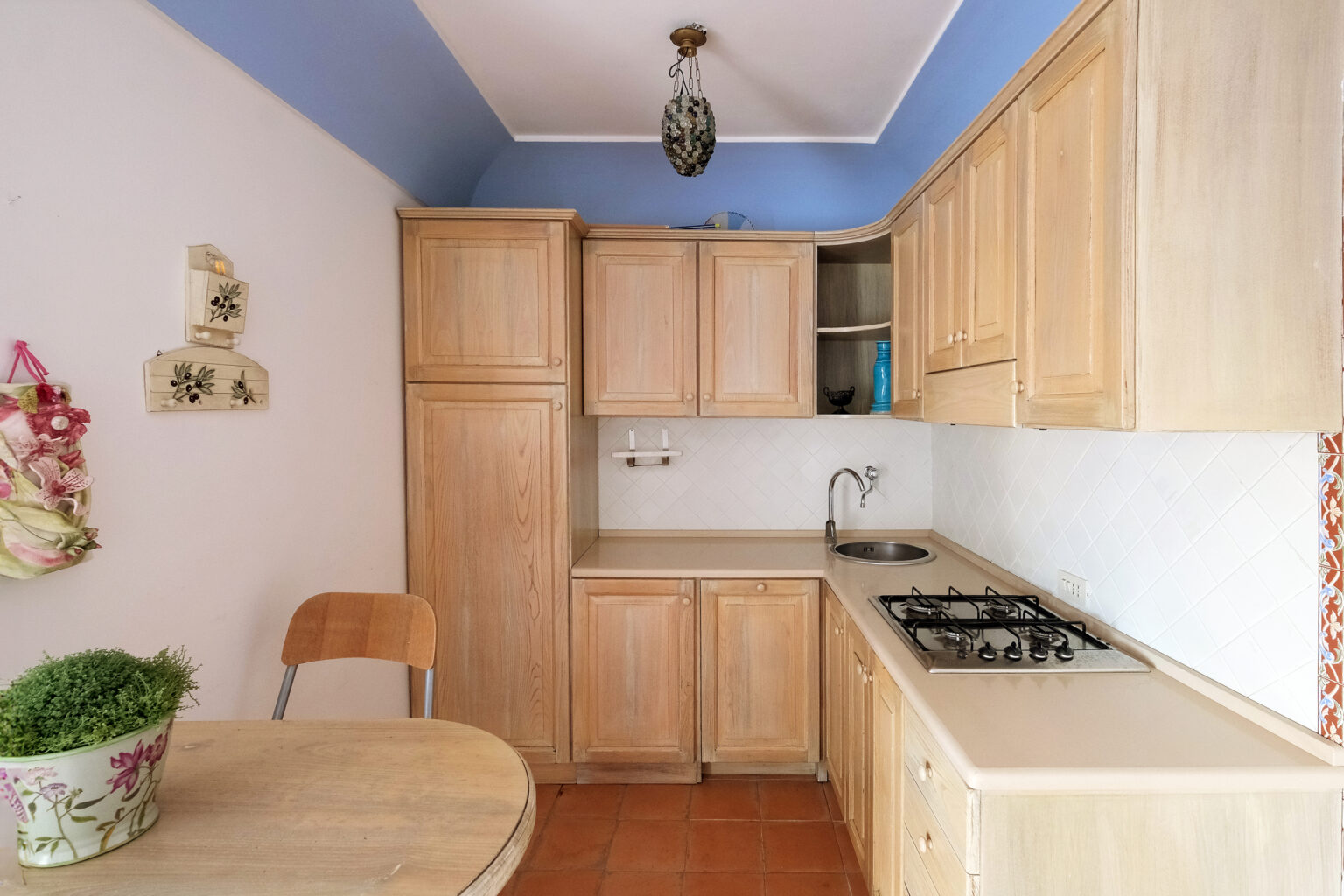 Cozy kitchen interior featuring light wooden cabinets, a gas stove, and a small dining table. The walls are painted in soft colors with a decorative touch, creating a warm atmosphere. | Only on SopranoVillas