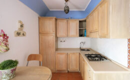 Cozy kitchen interior featuring light wooden cabinets, a gas stove, and a small dining table. The walls are painted in soft colors with a decorative touch, creating a warm atmosphere.