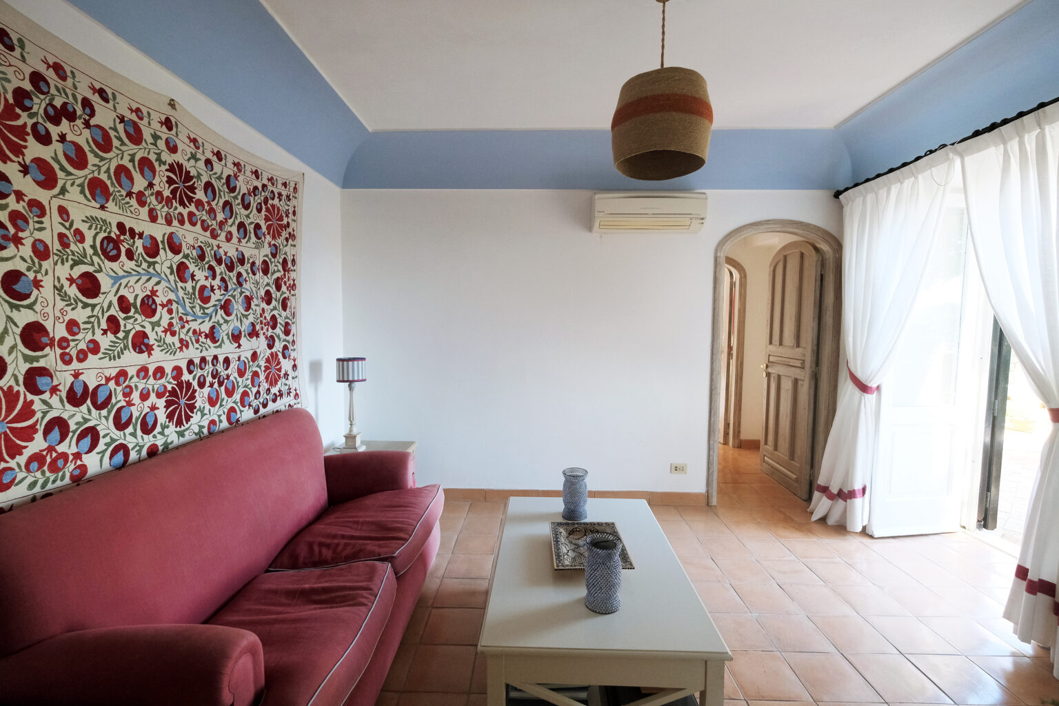 Living room featuring a red sofa, decorative wall art, and large windows with sheer curtains, creating a bright and inviting atmosphere. | Only on SopranoVillas