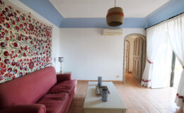Living room featuring a red sofa, decorative wall art, and large windows with sheer curtains, creating a bright and inviting atmosphere.
