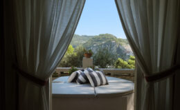 Cozy outdoor seating area with striped cushions, framed by sheer curtains, offering a scenic view of lush hills and clear blue sky. Perfect for relaxation and enjoying nature.