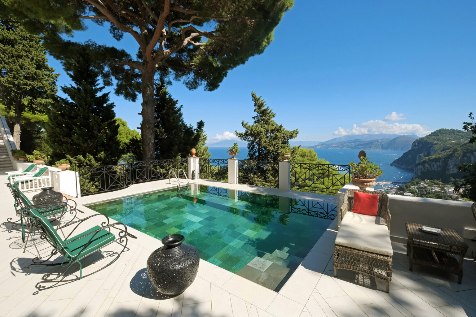 Luxurious villa pool overlooking a stunning coastal view, surrounded by lush greenery and stylish outdoor seating. Ideal for relaxation and enjoying scenic landscapes. | Only on SopranoVillas