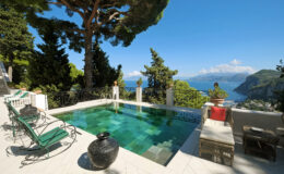 Luxurious villa pool overlooking a stunning coastal view, surrounded by lush greenery and stylish outdoor seating. Ideal for relaxation and enjoying scenic landscapes.