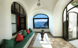 Modern coastal living room with arched windows offering a stunning ocean view, featuring a minimalist design, white walls, and a comfortable seating area adorned with colorful cushions.