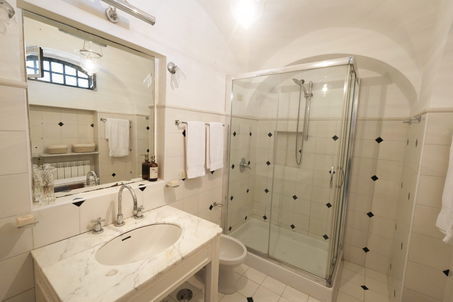 Modern bathroom featuring a glass shower enclosure, marble sink countertop, and elegant mirror. The space is well-lit with neutral-colored tiles and towels neatly arranged, creating a clean and stylish atmosphere. | Only on SopranoVillas
