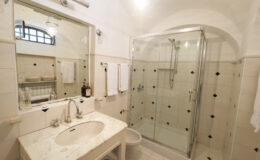 Modern bathroom featuring a glass shower enclosure, marble sink countertop, and elegant mirror. The space is well-lit with neutral-colored tiles and towels neatly arranged, creating a clean and stylish atmosphere.