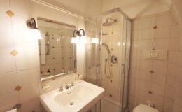 Modern bathroom featuring a glass shower enclosure, a white sink with chrome fixtures, and a large mirror, all set against tiled walls with decorative accents. Soft lighting enhances the clean and inviting atmosphere.