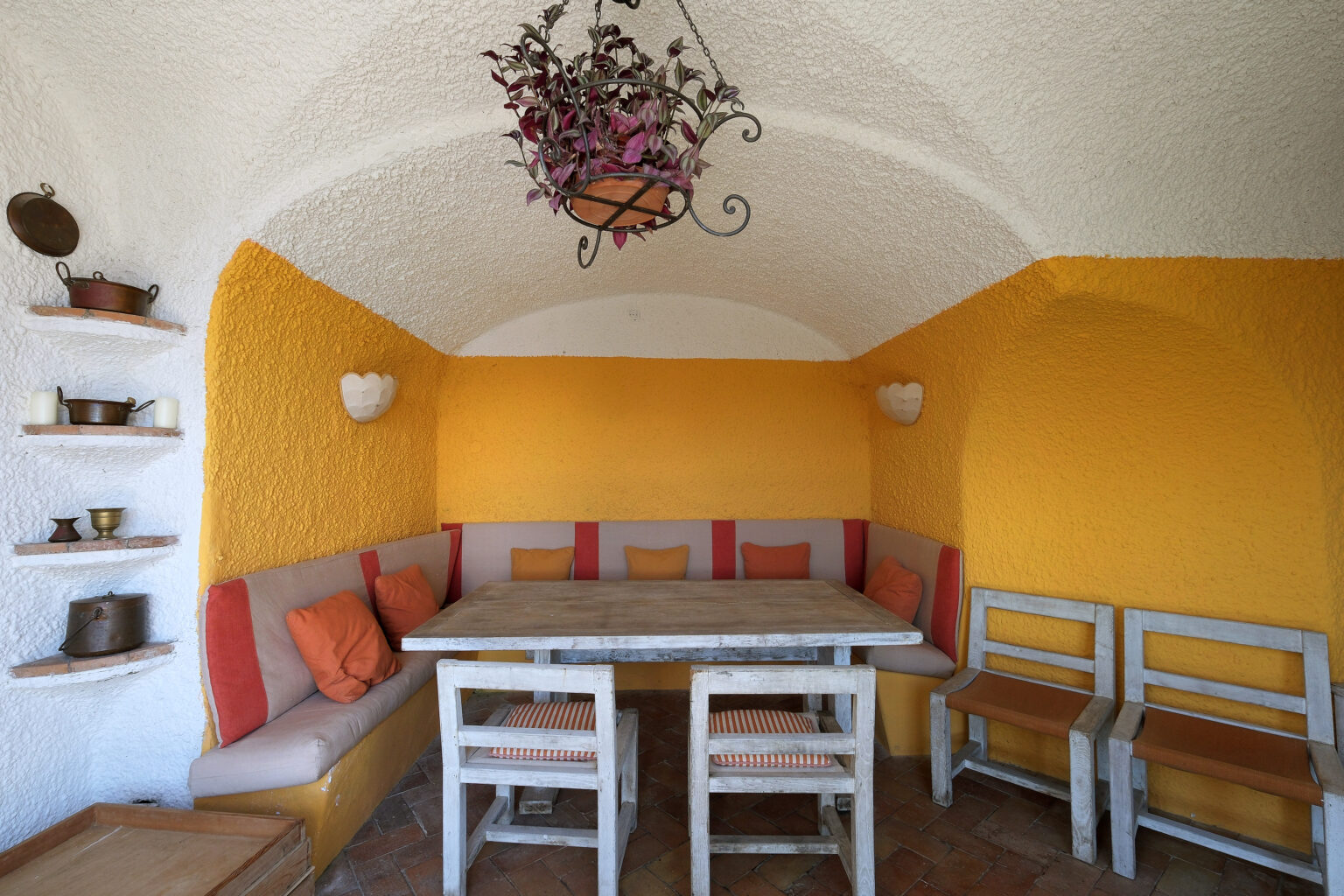 Cozy interior of a dining area featuring a rustic table and comfortable seating with orange and neutral tones, accented by decorative wall shelves and a stylish chandelier. Ideal for gatherings and relaxation. | Only on SopranoVillas