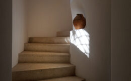 A serene staircase with natural stone steps, illuminated by soft sunlight filtering through a window, showcasing a decorative clay pot at the top.