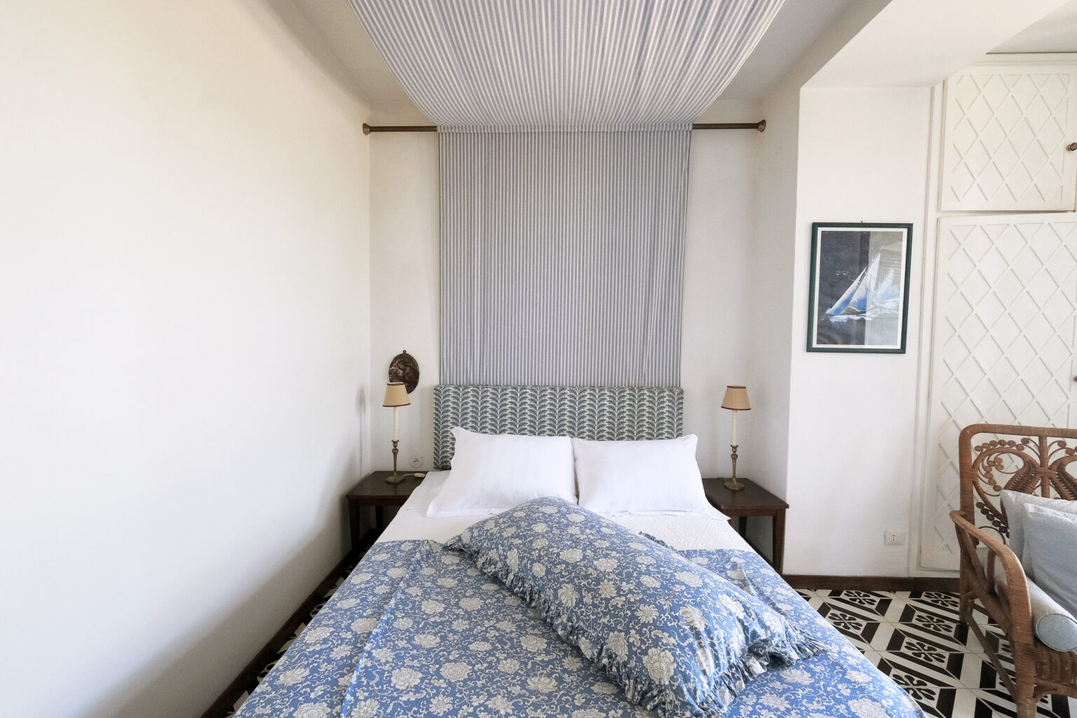 Cozy bedroom featuring a double bed with blue floral bedding, soft lighting from bedside lamps, and a minimalist aesthetic. The room has a light-colored wall and a decorative wall hanging, creating a serene atmosphere. Ideal for relaxation and comfort. | Only on SopranoVillas