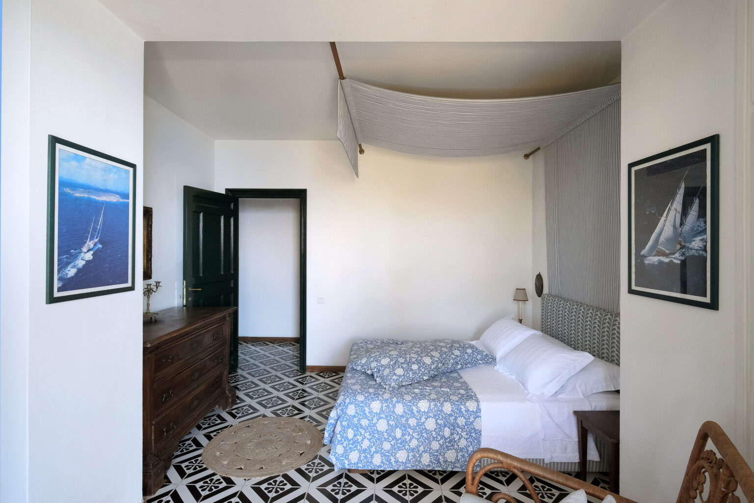 Cozy bedroom featuring a double bed with blue and white bedding, wooden furniture, and nautical-themed artwork on the walls. The room is well-lit, showcasing a blend of modern and classic design elements. | Only on SopranoVillas